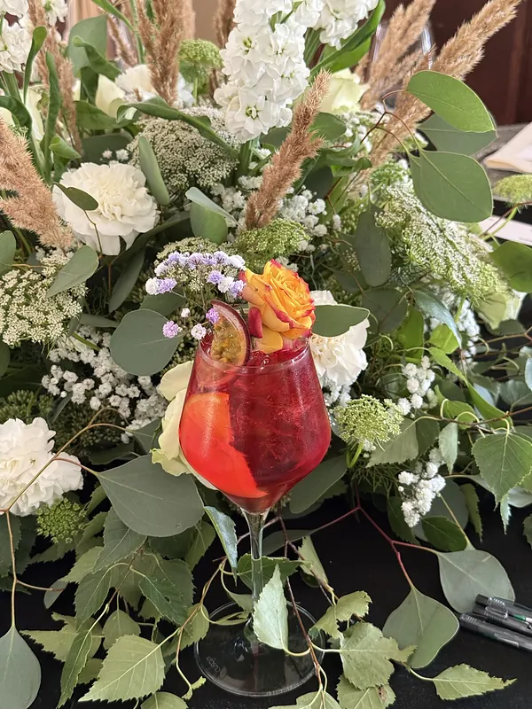 Raudonas kokteilis su pasiflora tarp gėlių kompozicijos